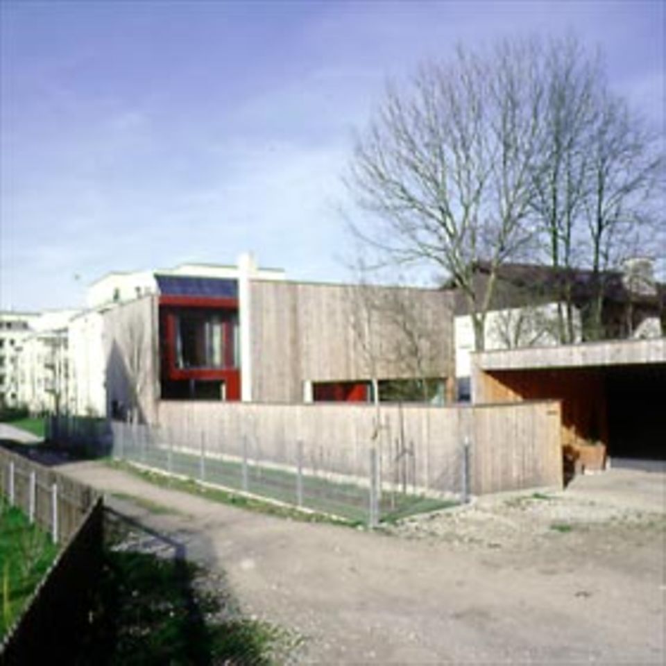 Haus Kammerl im vorstädtischen München geht auf Distanz zu der disparaten Umgebung. Es ist um einen Lichthof gruppiert, dessen rote Wände das Holz der Fassade kontrastieren.