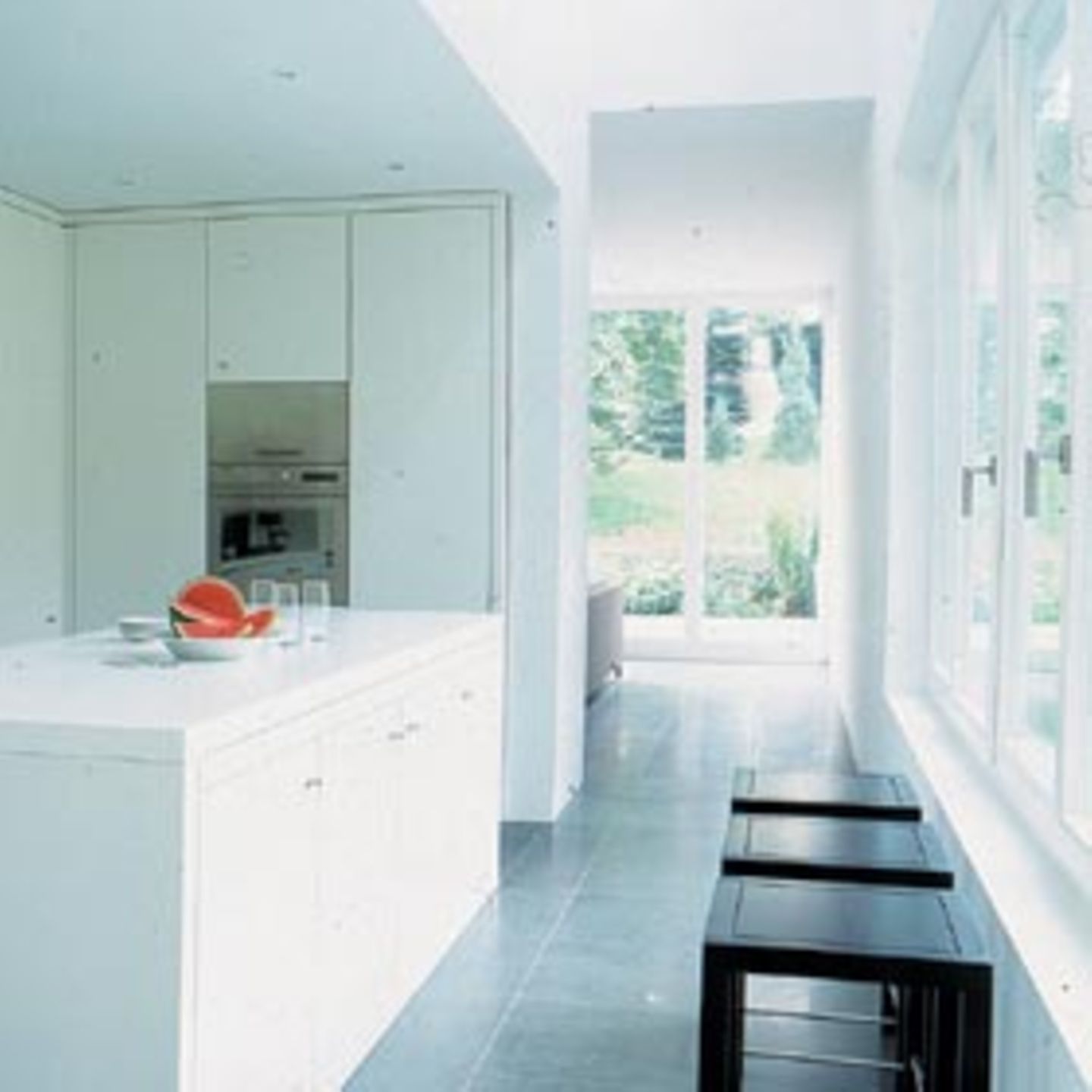 Die Bauherren legten Wert auf Einbaumöbel. Die schlichte weiße Küche liegt in einem zentralen Block zwischen Wohn- und Essbereich. Von beiden Schmalseiten des Hauses sieht man durch große Glasflächen ins Grüne.