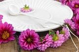 Lilafarbene Dahlienblüten um einen weißen Teller