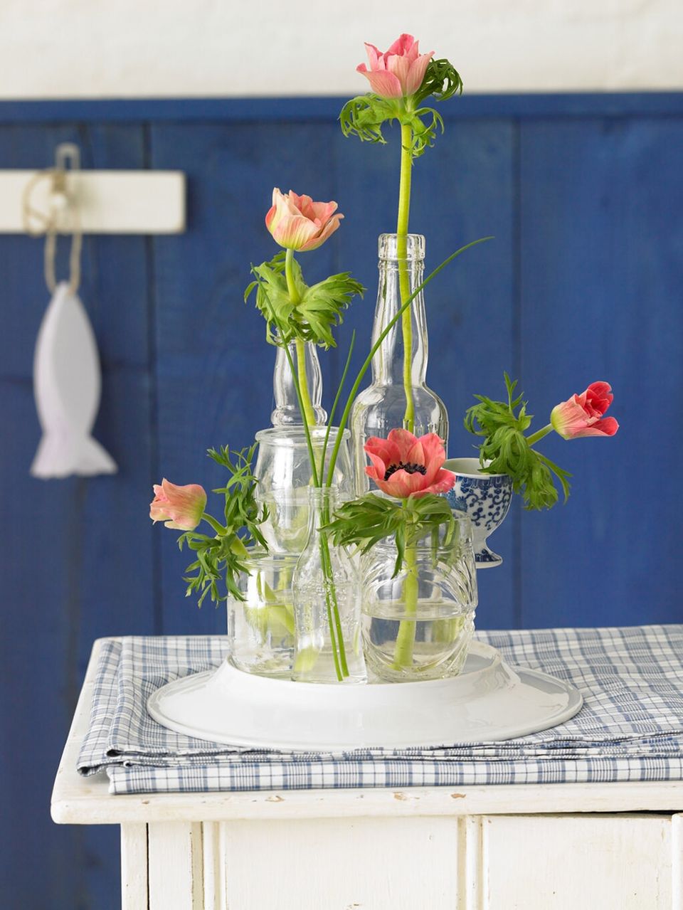 Glasflaschen und Gläser als improvisierte Vase auf einem Teller arrangiert