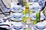 Gedeckter Tisch mit weißem Geschirr und schwarzen, grünen und goldenen Accessoires