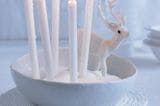 Winterliche Schneedeko mit Kerzen und einem Glitzerhirsch