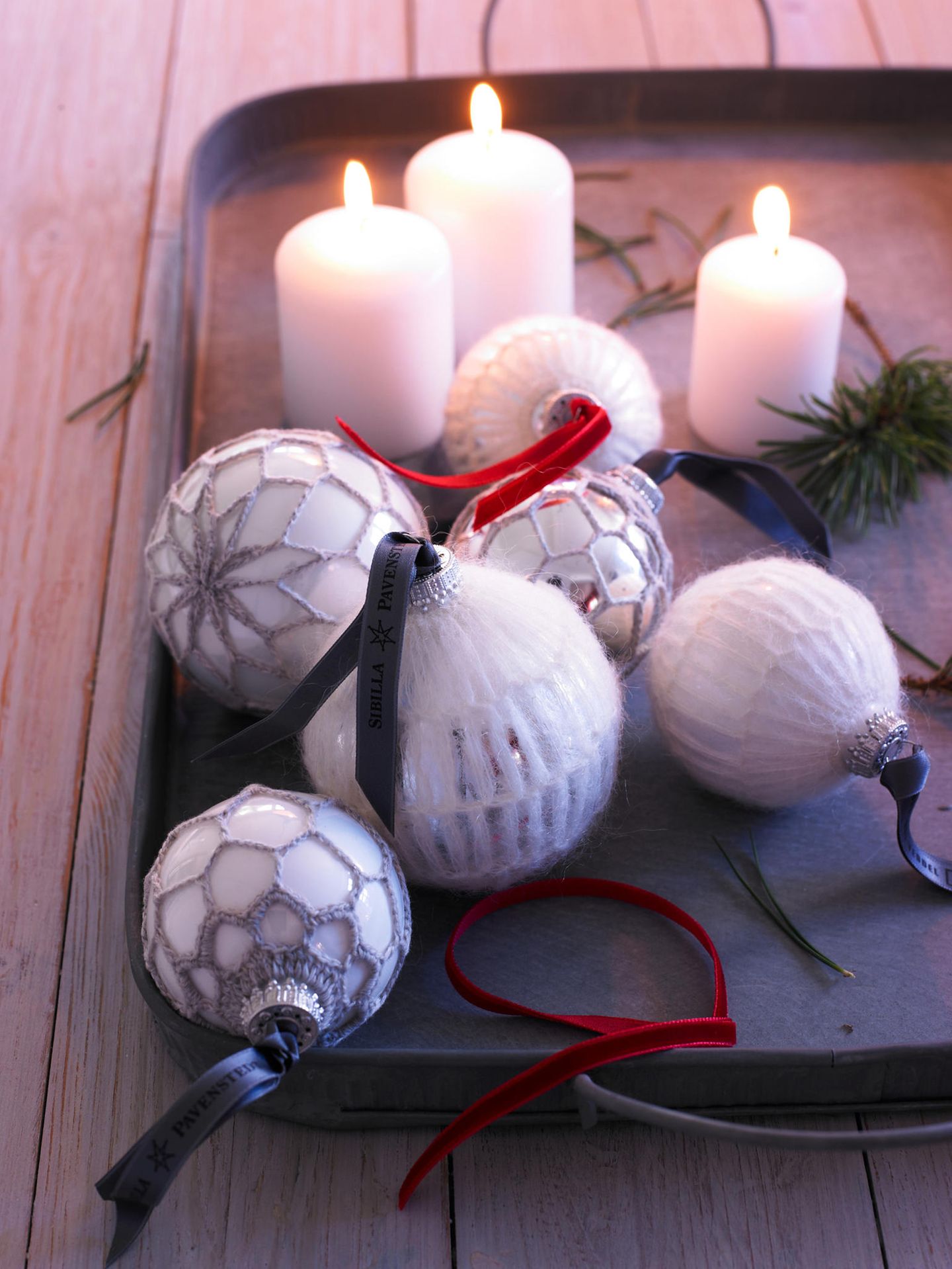 Umhäkelte Weihnachtskugeln auf einem Tablett mit Kerzen
