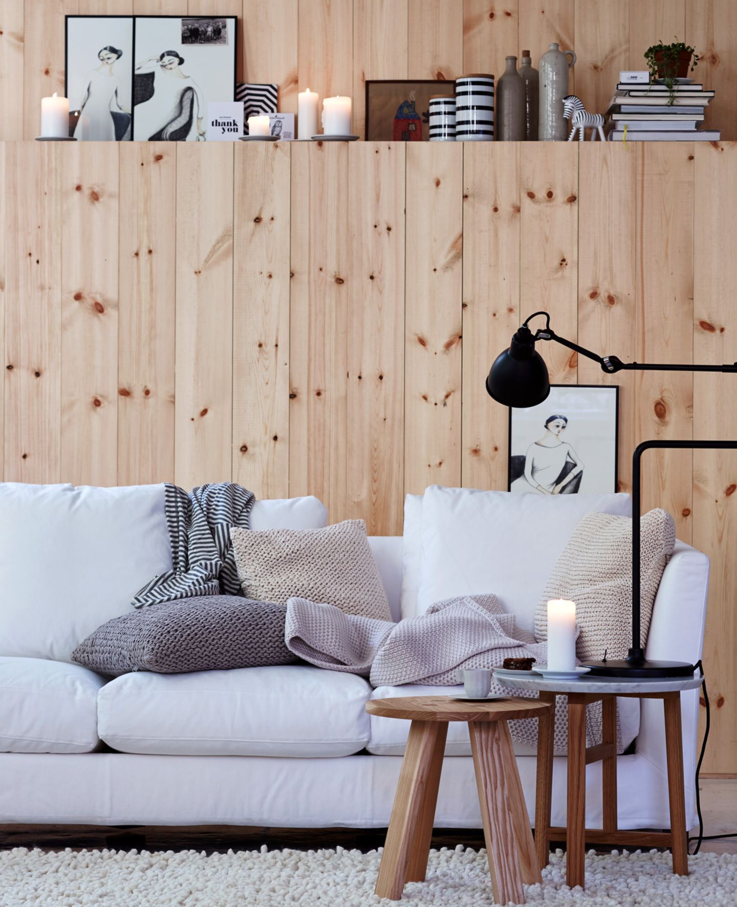 Sofa in Weiß, Wandvertäfelung aus Holz, Beistelltische aus Holz und gestrickte Kissenhüllen