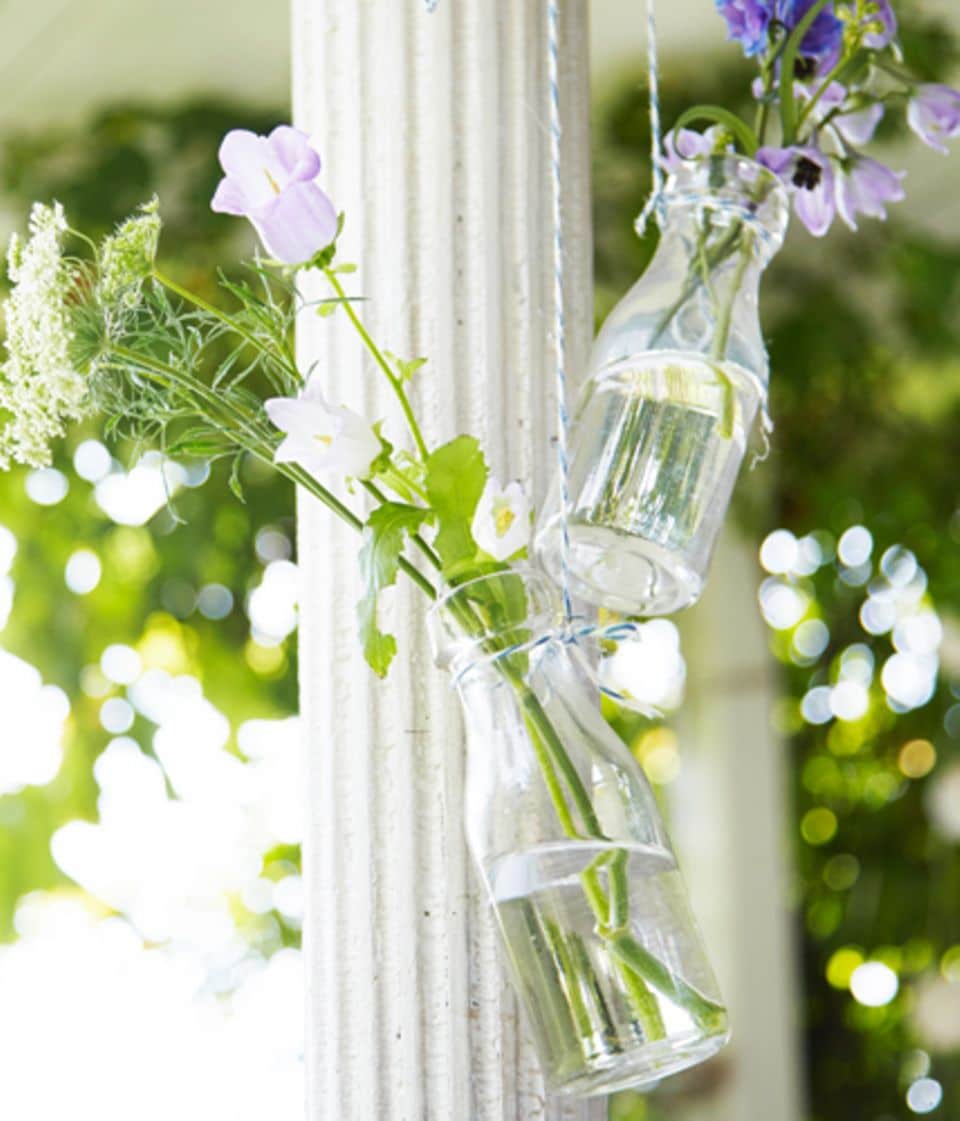 Die schönste Deko sind selbstgepflückte Blumen - und die müssen nicht nur auf dem Tisch stehen. Einfach in kleine Glasflaschen stellen und mit einem kräftigen Garn aufhängen.