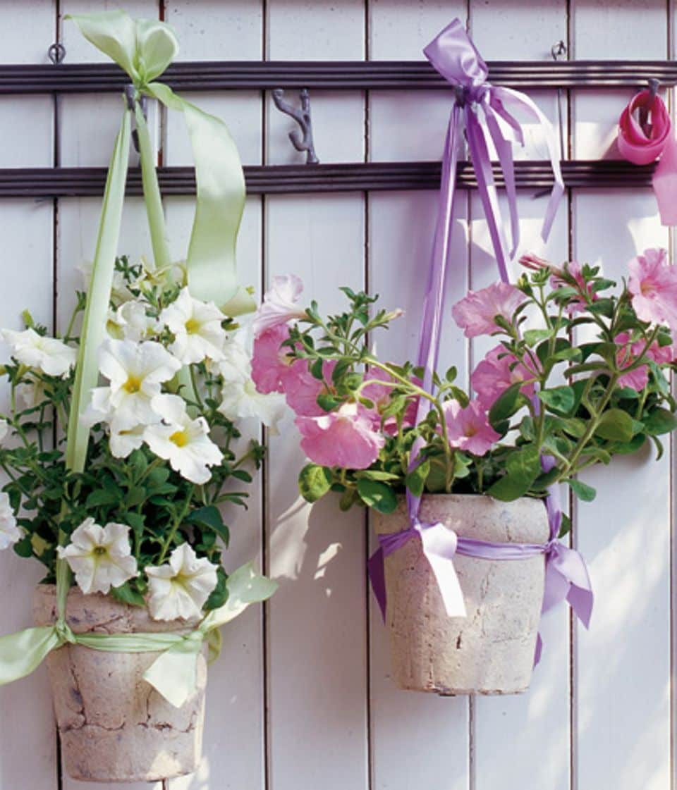 Kein Platz für Balkonpflanzen? Hängen Sie Töpfe mit Petunien und anderen Pflanzen doch mit hübschen Bändern an eine sonnige Wand.