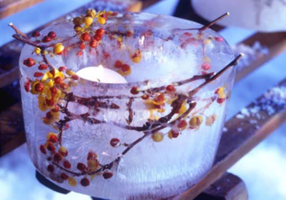 Ein Teelicht im Inneren der Eisskulptur verbreitet stimmungsvolles Licht. Ein paar Zweige und die bunten Beeren des Baumwürgers ragen aus dem Rand der Laterne.
