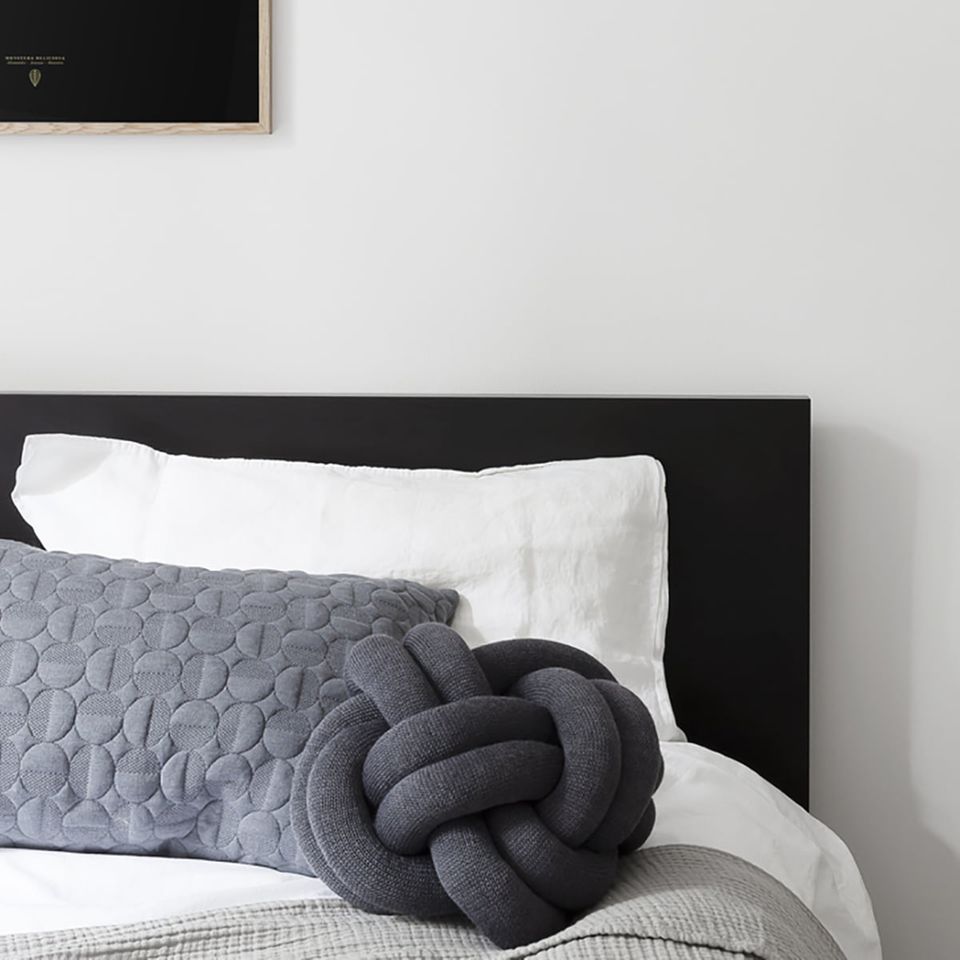 Schwarzes Kissen "Knot" auf Bett mit weißer Bettwäsche