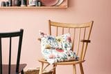 Rosa Wandfarbe mit Holzstühlen und geblümten Kissen