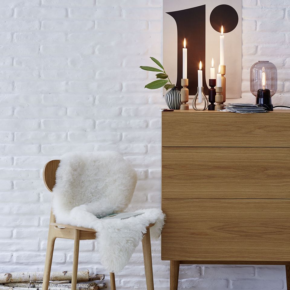 Gemütlich wohnen: Kommode, Stuhl und Kerzenhalter aus Holz mit Fell und Kerzen