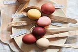 Mit natürlichen Zutaten gefärbte Eier auf einem Teller und Holzlöffeln