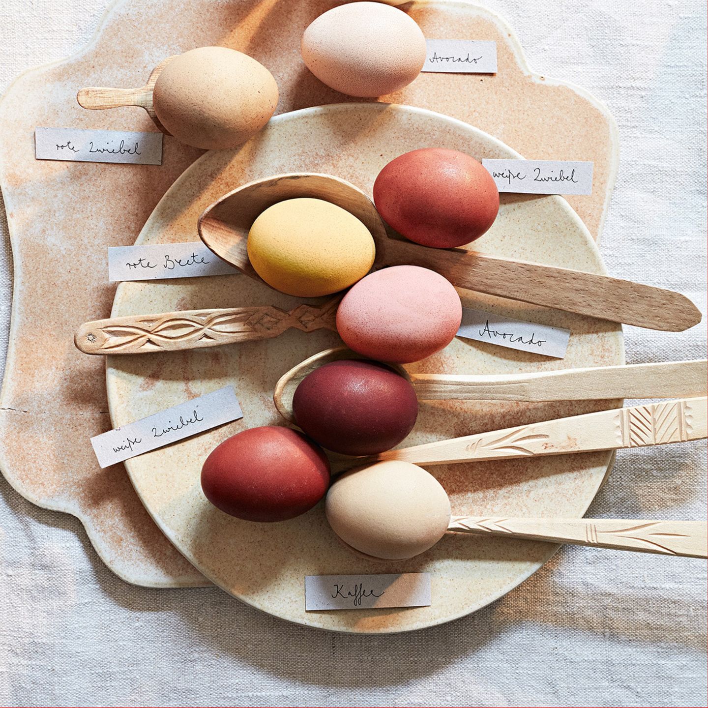 Mit natürlichen Zutaten gefärbte Eier auf einem Teller und Holzlöffeln