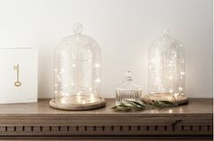 Zwei mit Lichterketten geschmückte Glaskugeln von Lights4fun auf einer Holzablage