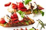 Crostini mit Antipasti und Burrata auf hellem Untergrund