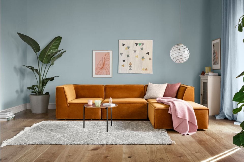 Sofa in leuchtendem Ocker vor taubenblauer Wand