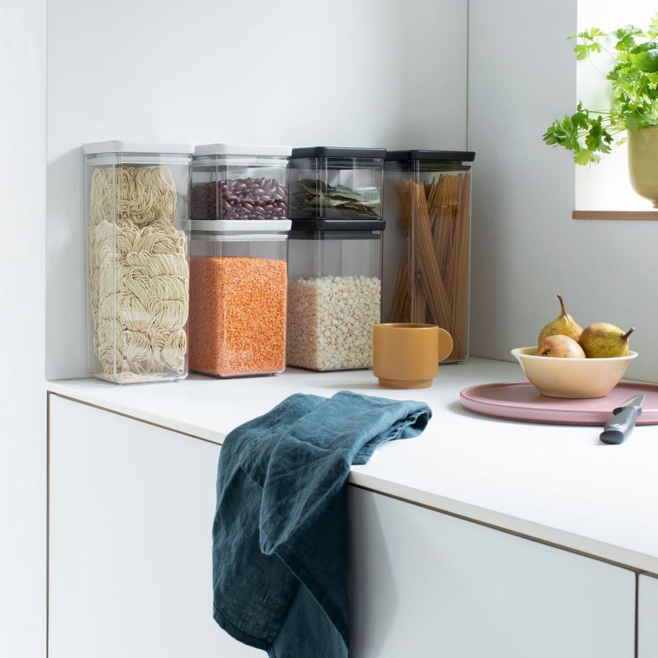 Durchsichtige Vorratsdosen mit unterschiedlichen Trockenlebensmitteln in einer weißen Küche gestapelt
