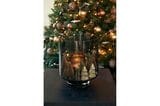 Weihnachtlich dekoriertes Hurricane Glas vor einem geschmückten Weihnachtsbaum
