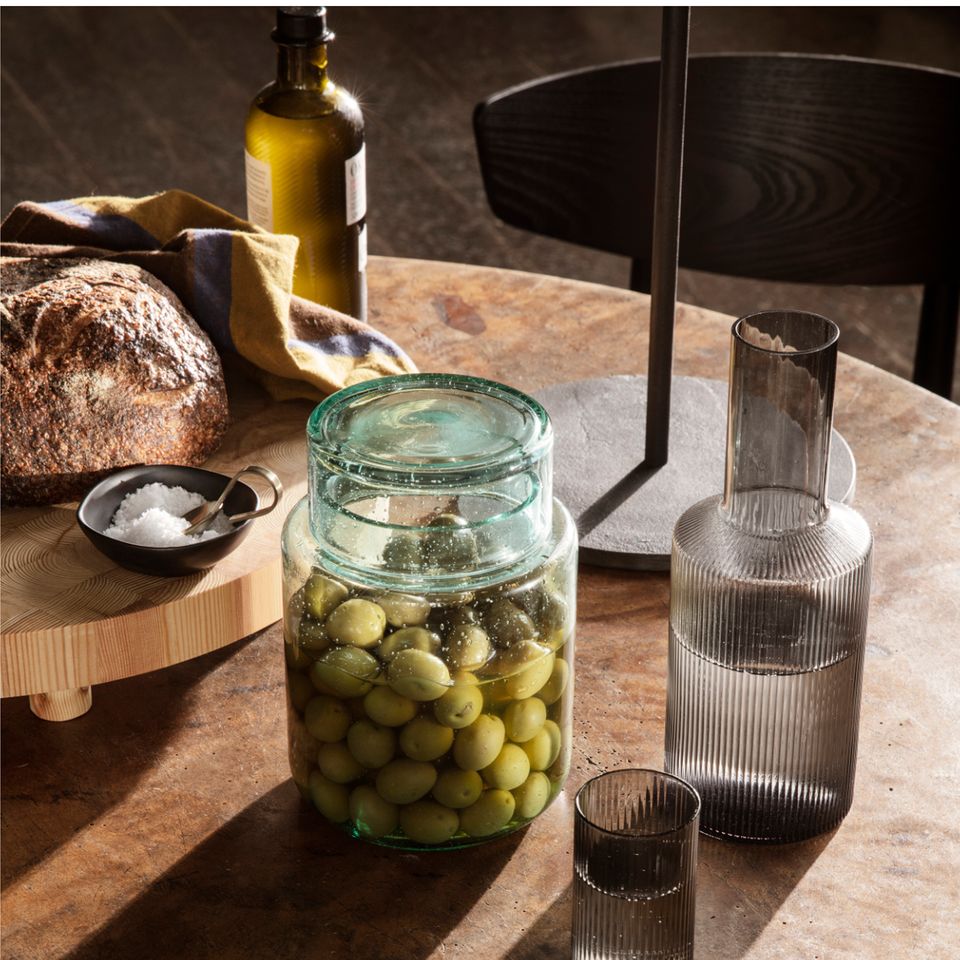 Großes Glas mit Deckel gefüllt mit grünen Oliven auf dem Tisch