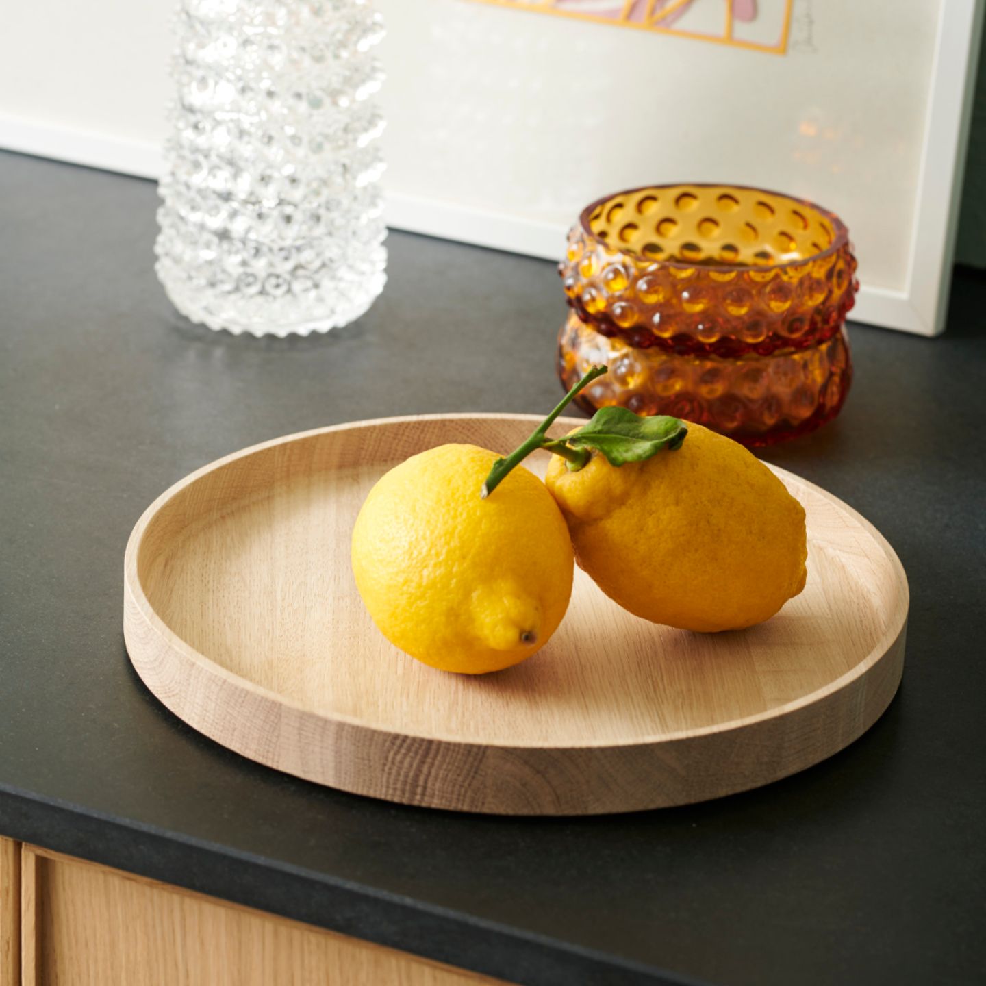 Holztablett mit zwei Zitronen drauf, dahinter stehen zwei dekorative Glasgefäße