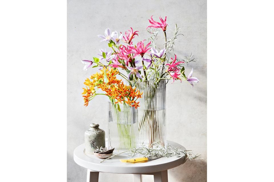 Winterstrauß mit bunt blühenden Clematis in durchsichtigen hohen Vasen