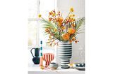 Winterstrauß in grün-weiß-gestreifter Vase mit orange- und gelbblühenden Blumen