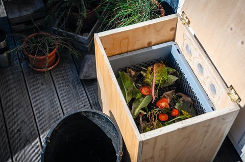 Eine geöffnete Wurmkiste mit Bioabfällen auf einer Terrasse stehend