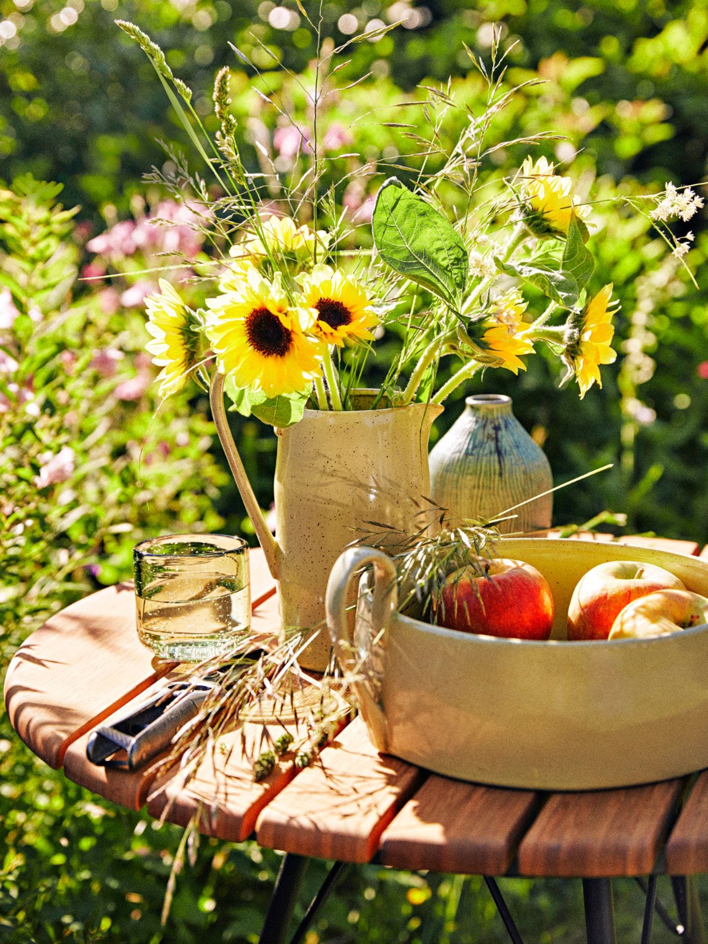 Kleiner runder Gartentisch mit Sonnenblumen und einer Schale mit Äpfel