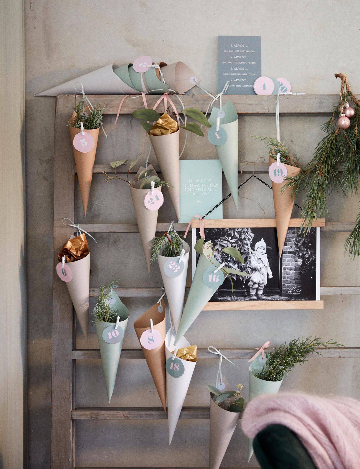 Adventskalender aus Tütchen in Pastelltönen hängen an einem Regal