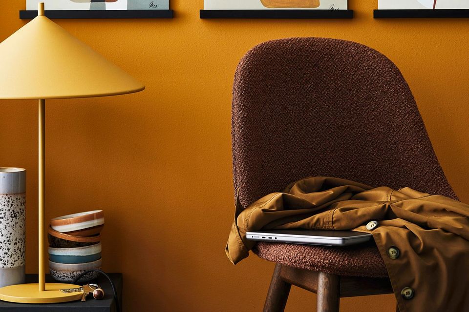 Ein brauner Stuhl steht vor einer ockerfarbenen Wand, die sich in der Lampe wiederfindet