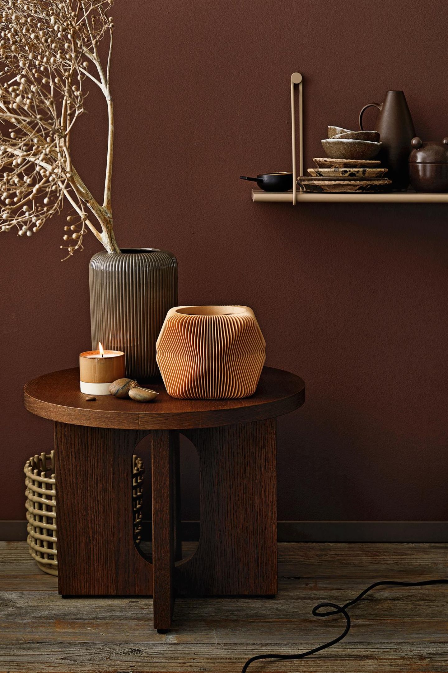 Ein Beistelltisch in dunklem Holz ist mit geriffelten Vasen und einer Kerze dekoriert; er steht vor einer dunkelbraunen Wand