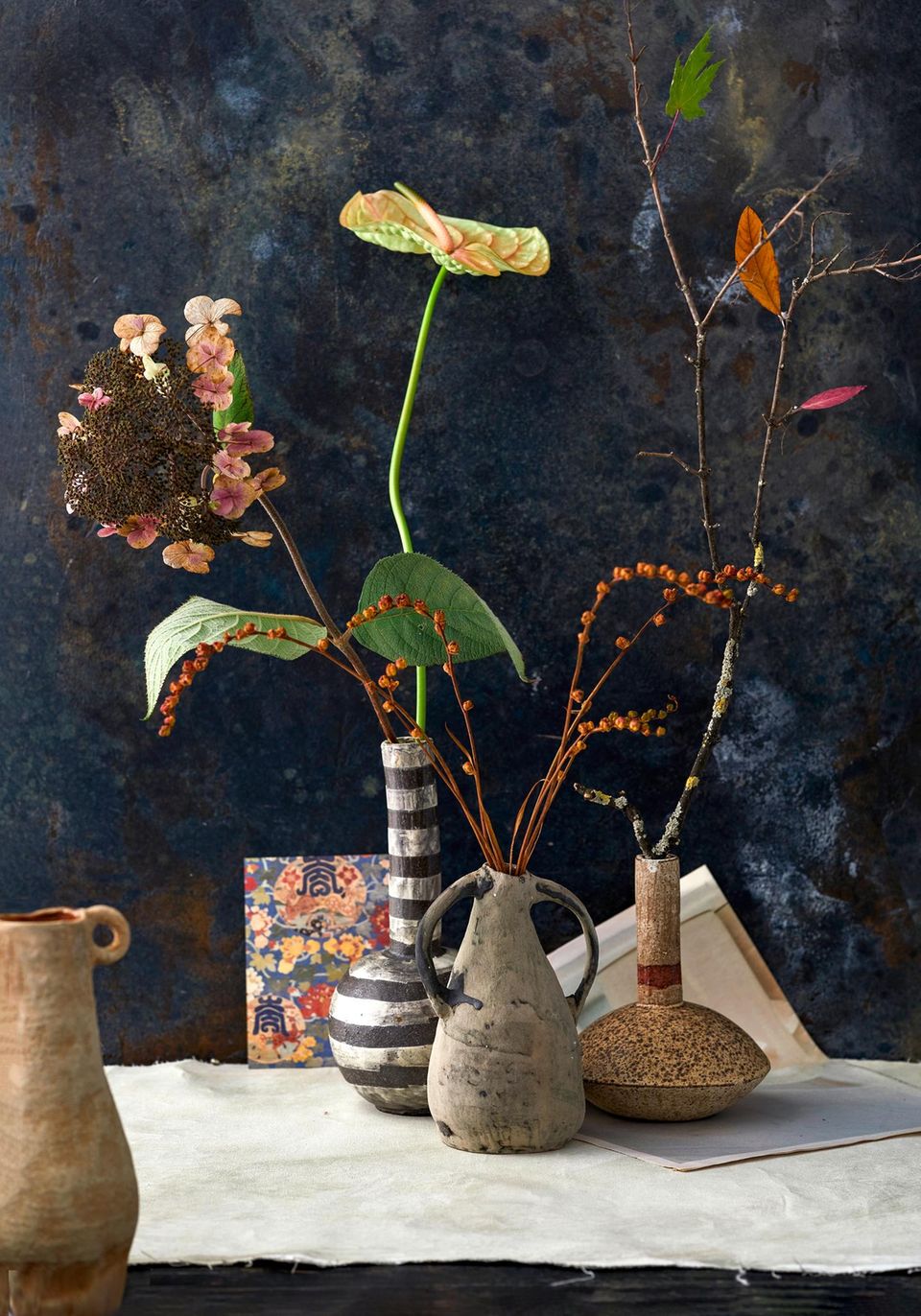 Blumen an langen Stielen ranken vor einem fast schwarzen Hintergrund aus dekorativen, rustikalen Vasen in die Höhe