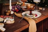 Rustikaler Weihnachtstisch mit Käsebrett und Trauben, erdfarbenem Geschirr und braunen Leinenservietten