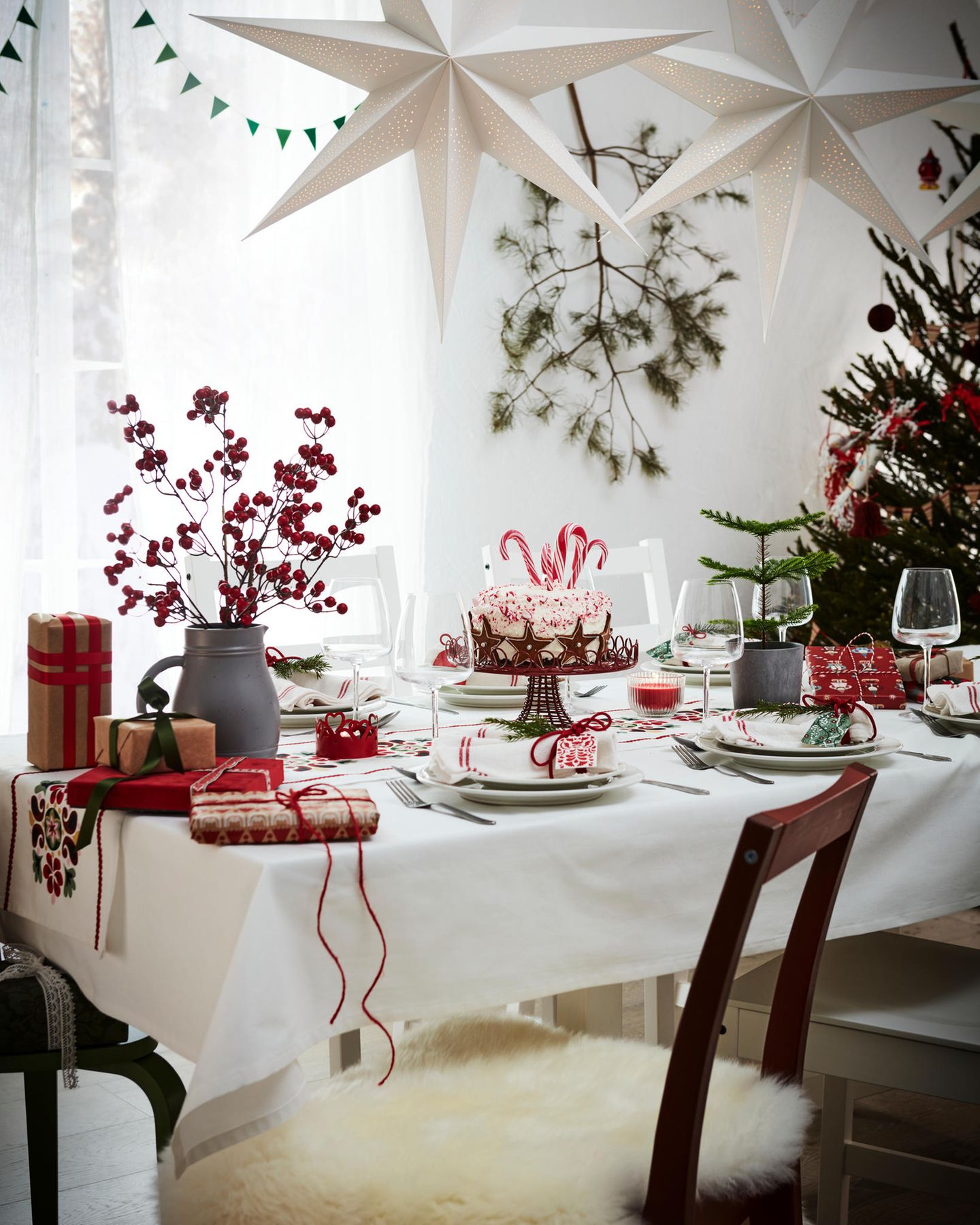 Weiße Tischdeko mit rot-weißen Servietten, weißem Geschirr und roten Beerenzweigen in einer grauen Vase