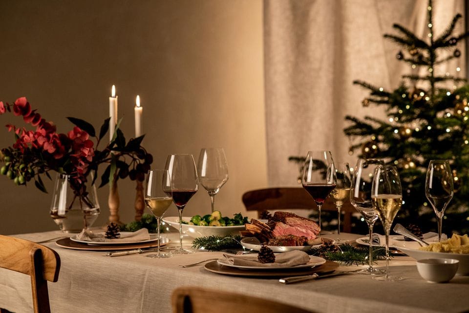 Tisch mit beiger Leinen-Tischdecke, Kerzenständern, Braten und Rosenkohl, ein Weihnachtsbaum im HG