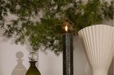 Kerze mit 24 Ziffern steht auf einer dunklen Anrichte vor einer organischen Vase mit grünen Zweigen.