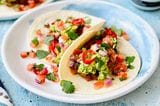 Zwei Tacos liegen gefüllt mit Salat, Tomaten und Avocado auf einem blau-weißen Teller