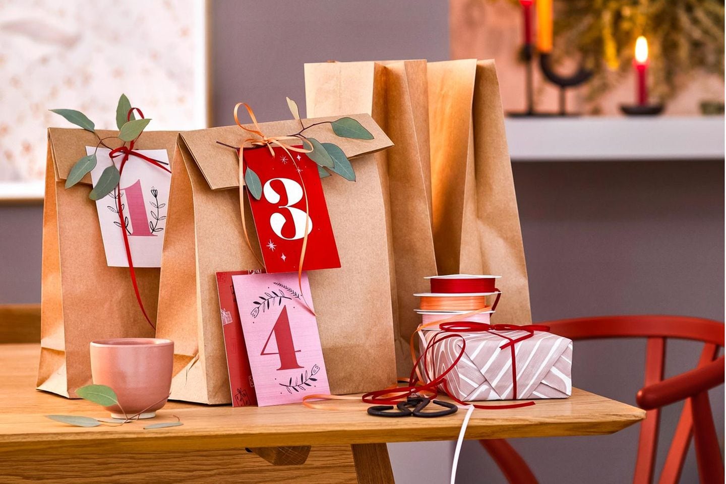 Adventstüten aus einfachem Papier mit weihnachtlichen Geschenkanhängern und Eukalyptuszweigen auf einem Holztisch