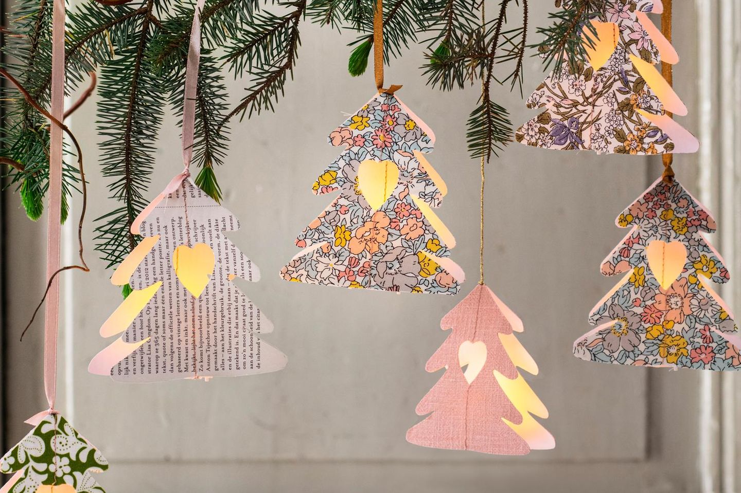 Weihnachtliche Baumlaternen aus Papier an Bändchen an Tannenzweigen herunterbaumelnd