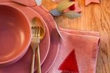 Keramik und Stoffserviette in Rosé sowie goldenes Besteck sind auf einem Holztisch arrangiert