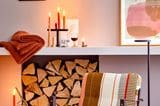 Gestreifter Sessel n gedeckten Farben steht in einem hellen Raum mit Kerzendeko und Korb voller Zapfen und Zweige