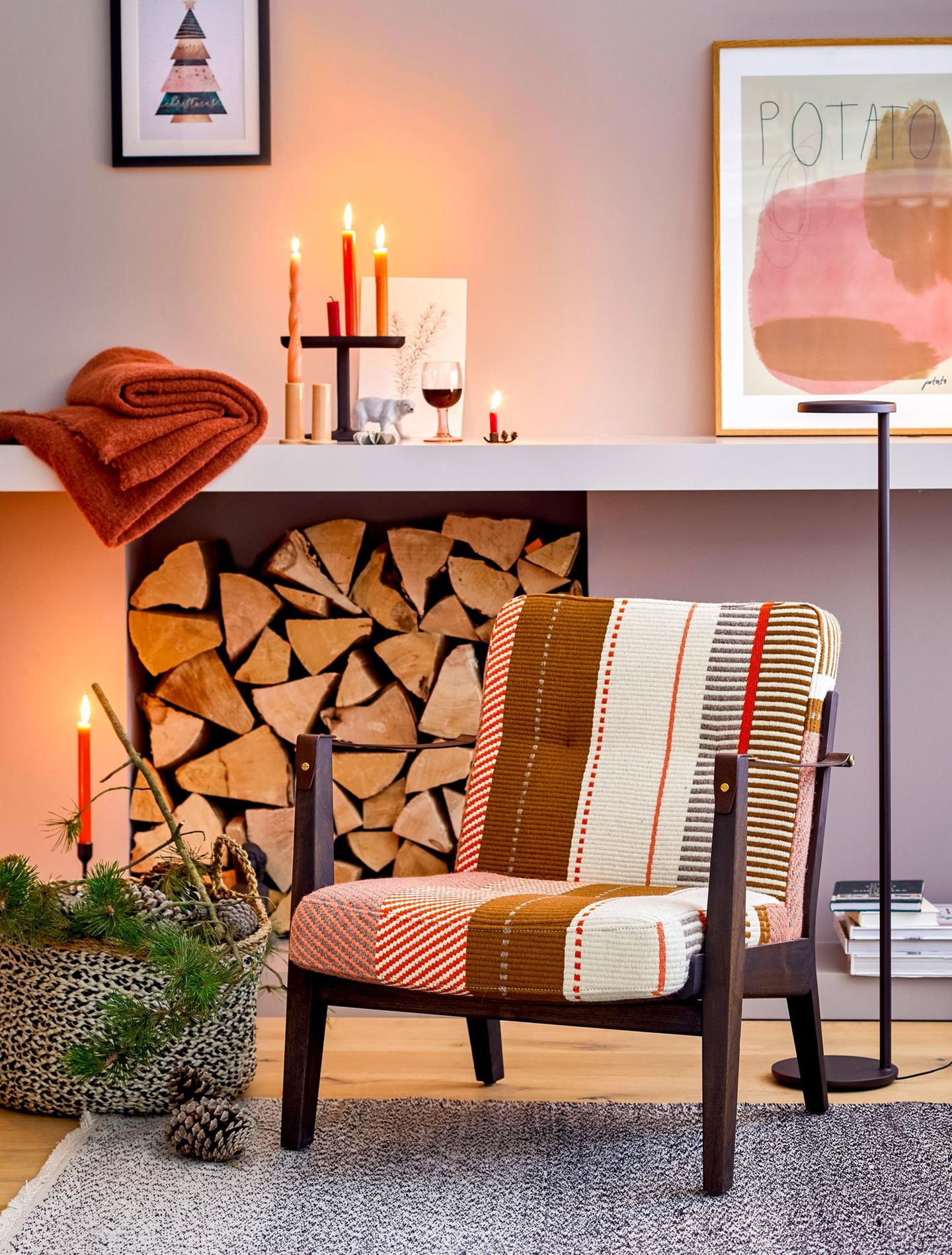 Gestreifter Sessel n gedeckten Farben steht in einem hellen Raum mit Kerzendeko und Korb voller Zapfen und Zweige