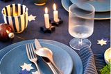 Blaue Keramik, sternförmige Kerzenhalter und schwarz-weiß gestreifte Becher stehen auf einer blauen Tischdecke