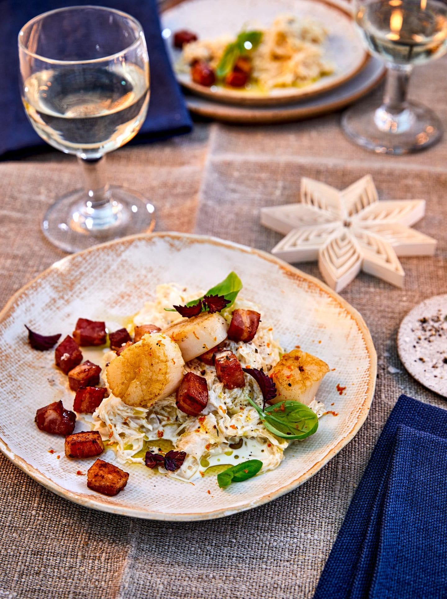 Auf einem festlich gedeckten Tisch mit Weingläsern, Sternen und blauen Servietten steht ein Teller mit Essen