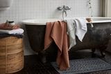 Alte Badewanne mit zwei Handtüchern über dem Rand liegend, daneben steht ein Wäschekorb