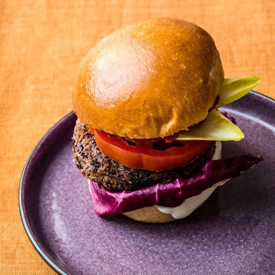Ein Burger mit veganem Bohnenpatty liegt auf einem violetten Teller