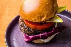 Ein Burger mit veganem Bohnenpatty liegt auf einem violetten Teller