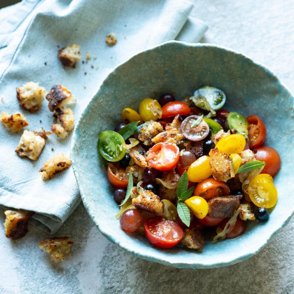 Salat mit bunten Mini-Tomaten, Trauben und Croûtons in einer blauen Keramikschüssel