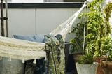 Eine weiße Hängematte mit grüner Decke auf einem Balkon mit Balkonpflanzen