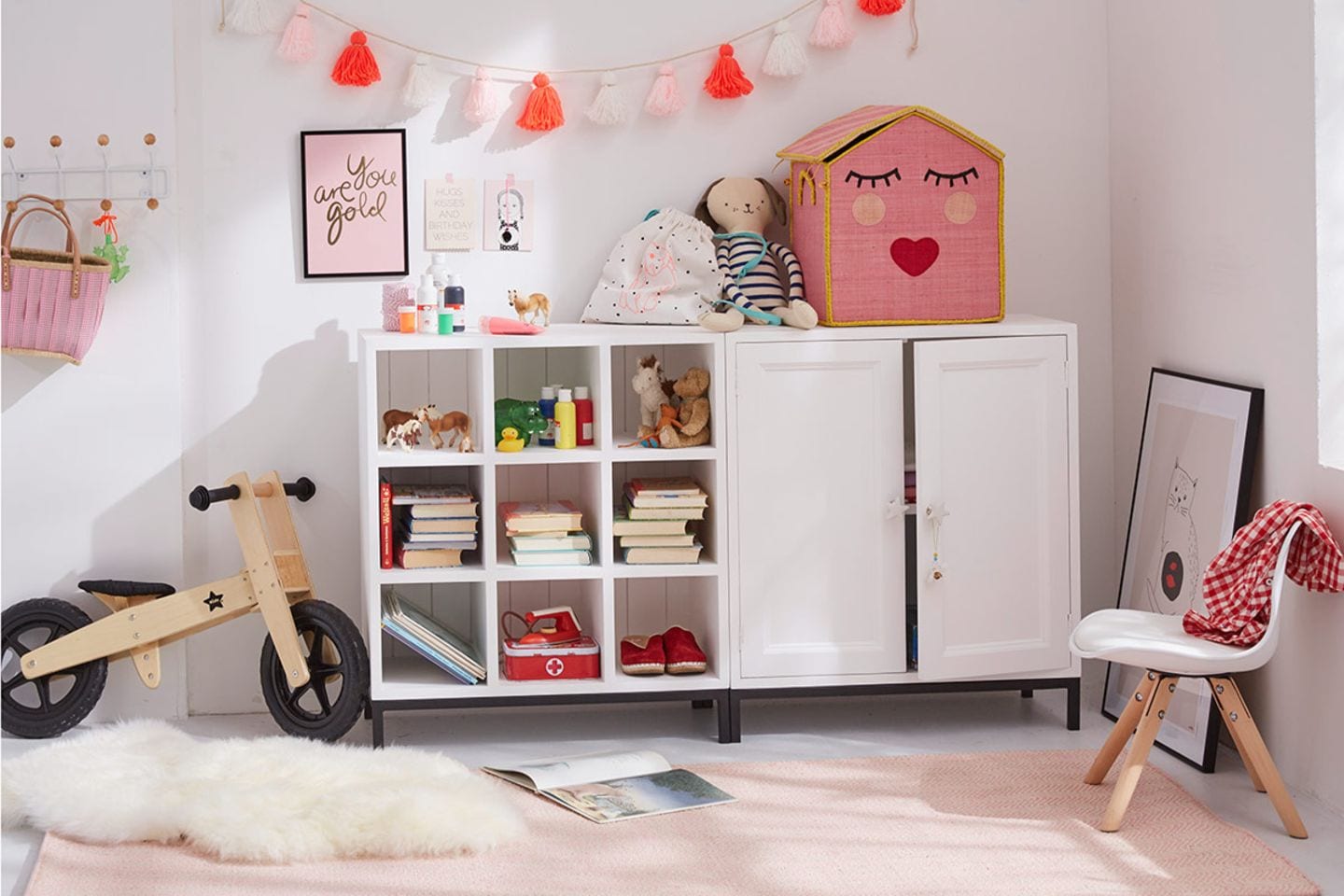 Mädchenzimmer mit weißer Kommode, Fellteppich, Laufrad, Wimpelkette und verschiedenen Spielsachen