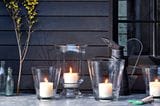 Gartentisch mit vier Kerzen in Vasen als Windlichter vor einer hölzernen Hauswand